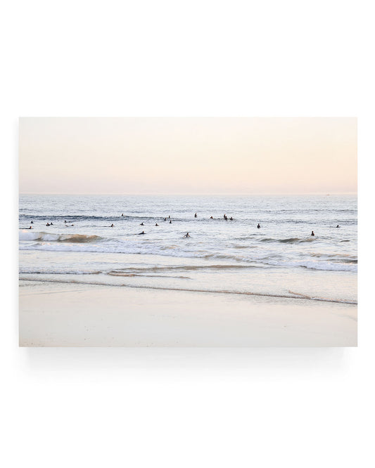 San Clemente surf wall art featuring surfers waiting in gentle ocean waves at sunset, with soft pastel sky tones and rolling waves along a sandy California shoreline.