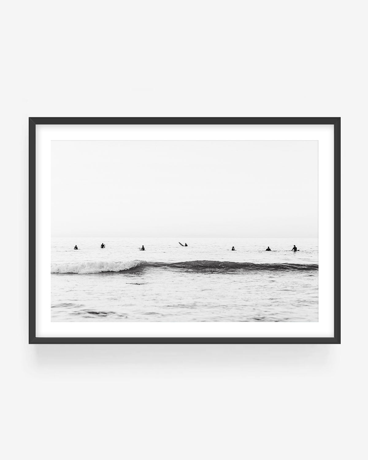 Black and white surf photography in black frame showing surfers waiting in calm ocean lineup, minimalist coastal wall art print.