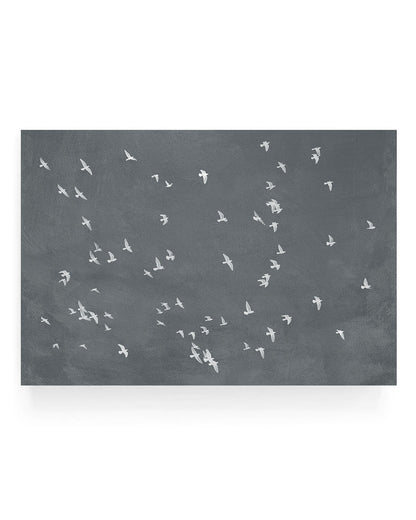 Minimalist graphite photograph of a flock of white birds flying across a dark gray sky, high contrast aerial bird silhouettes in motion.