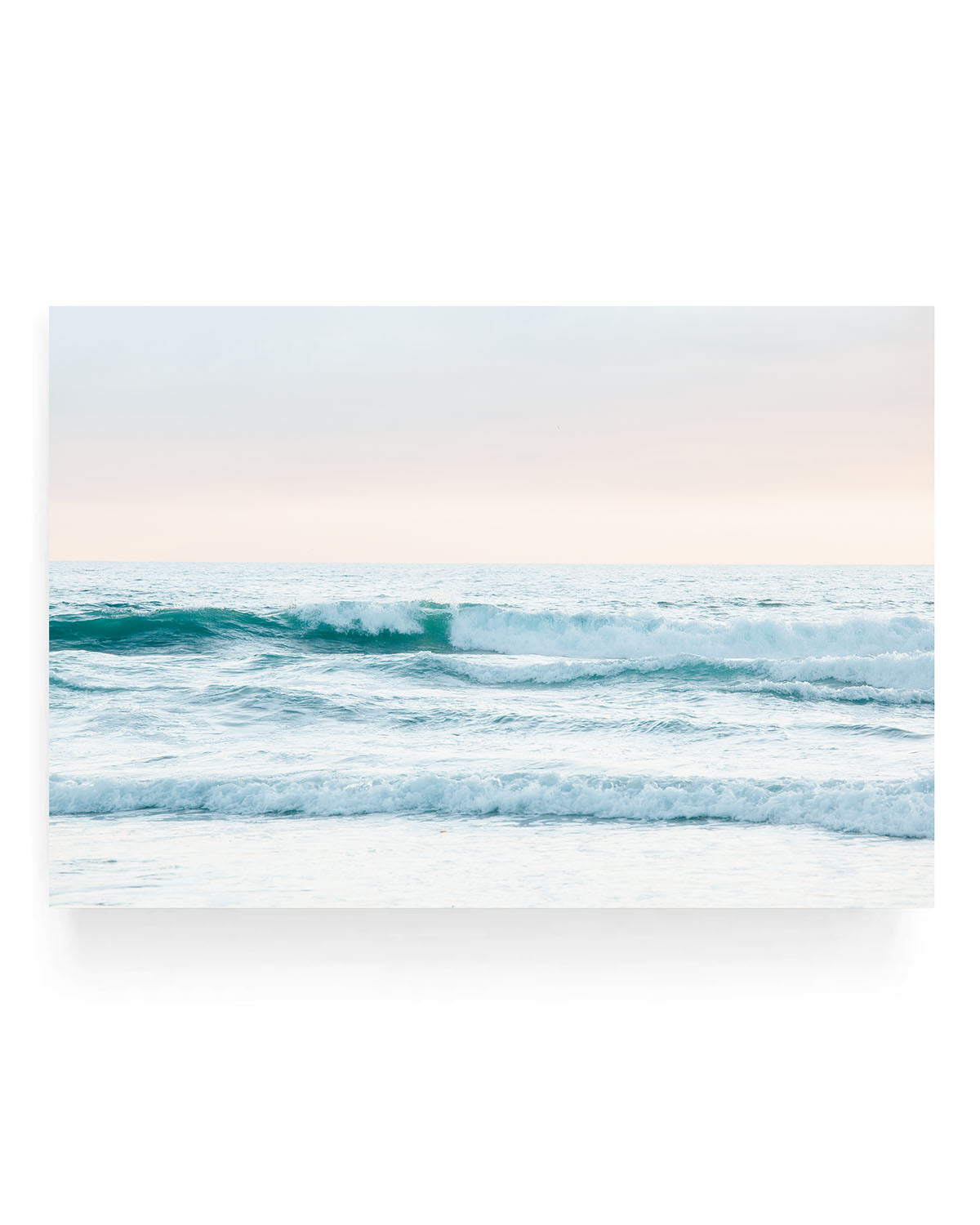 Rolling turquoise ocean waves breaking near the shoreline under a soft peach and blue sky at sunset, with textured water and gentle sea foam in view.