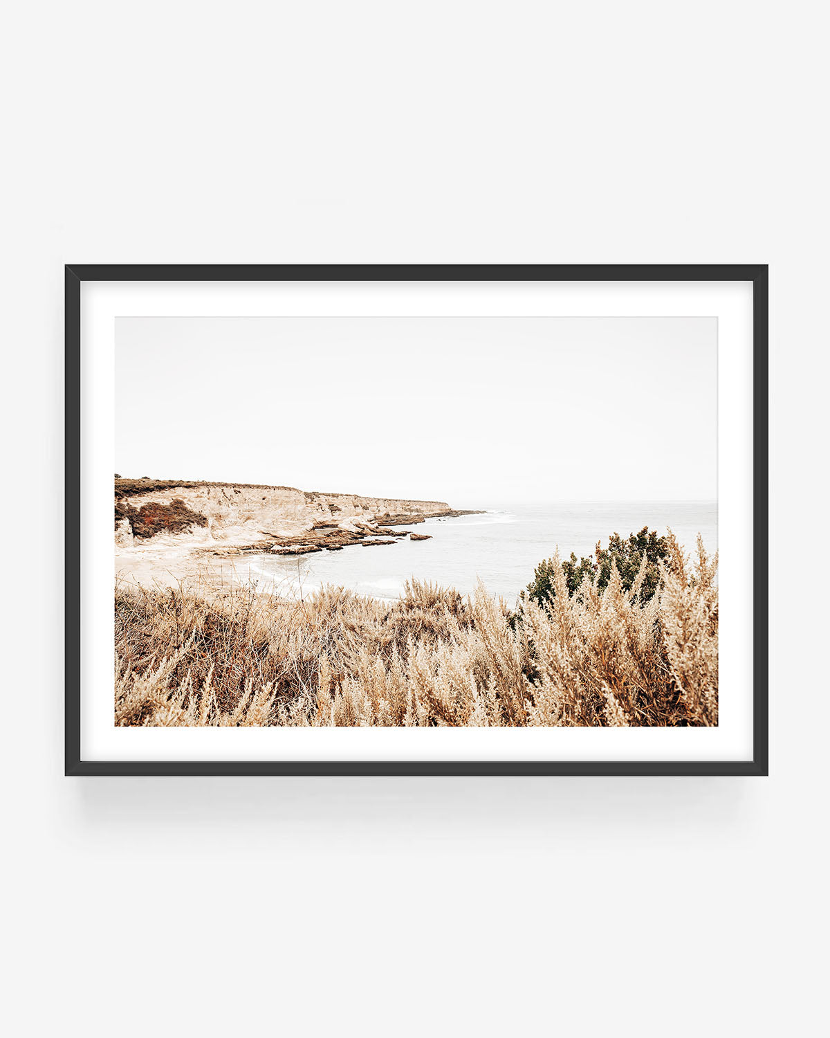 Coastal cliff landscape photography in black frame showing golden grasses and calm ocean, neutral coastal wall art print