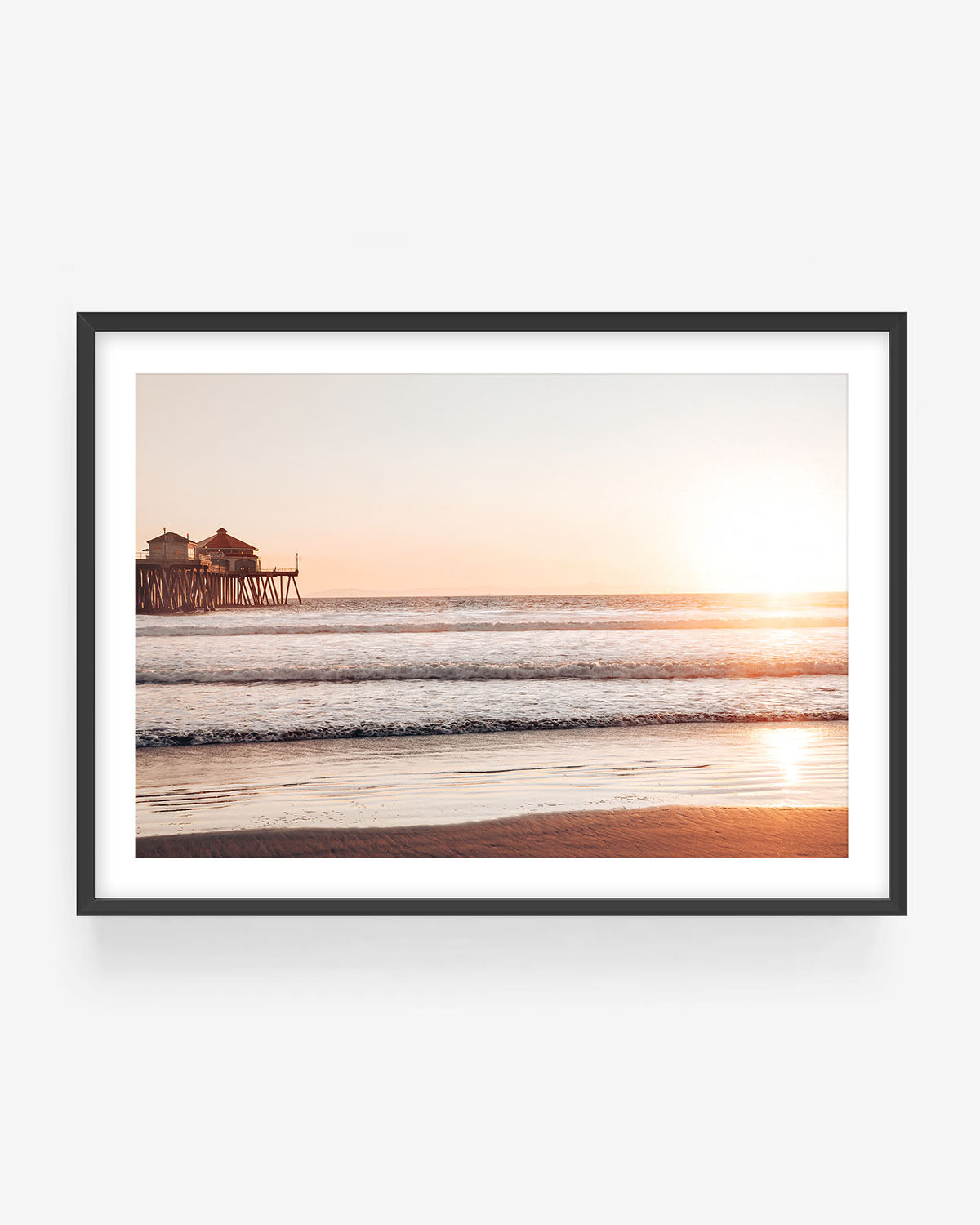 Huntington Beach sunset photography in black frame showing pier, waves, and golden light, coastal wall art print.