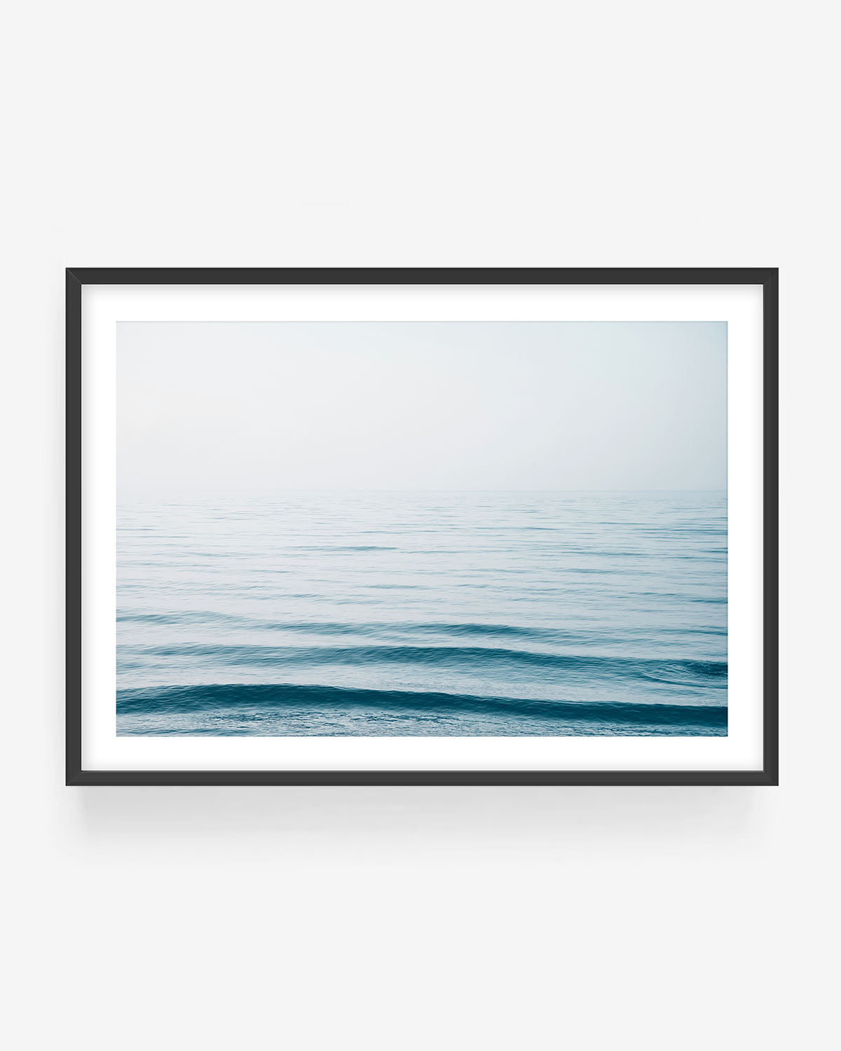 Minimalist ocean horizon photograph in black frame showing calm blue sea and soft sky, modern coastal wall art print.