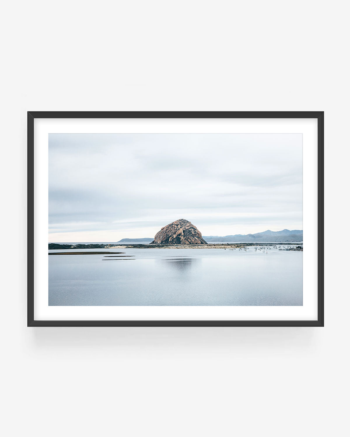 Morro Rock photography in black frame showing Morro Bay rock formation reflected in calm water with cloudy sky, minimalist California coastal wall art print.