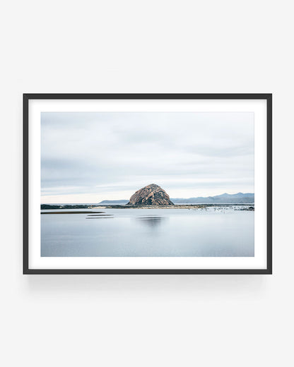 Morro Rock photography in black frame showing Morro Bay rock formation reflected in calm water with cloudy sky, minimalist California coastal wall art print.