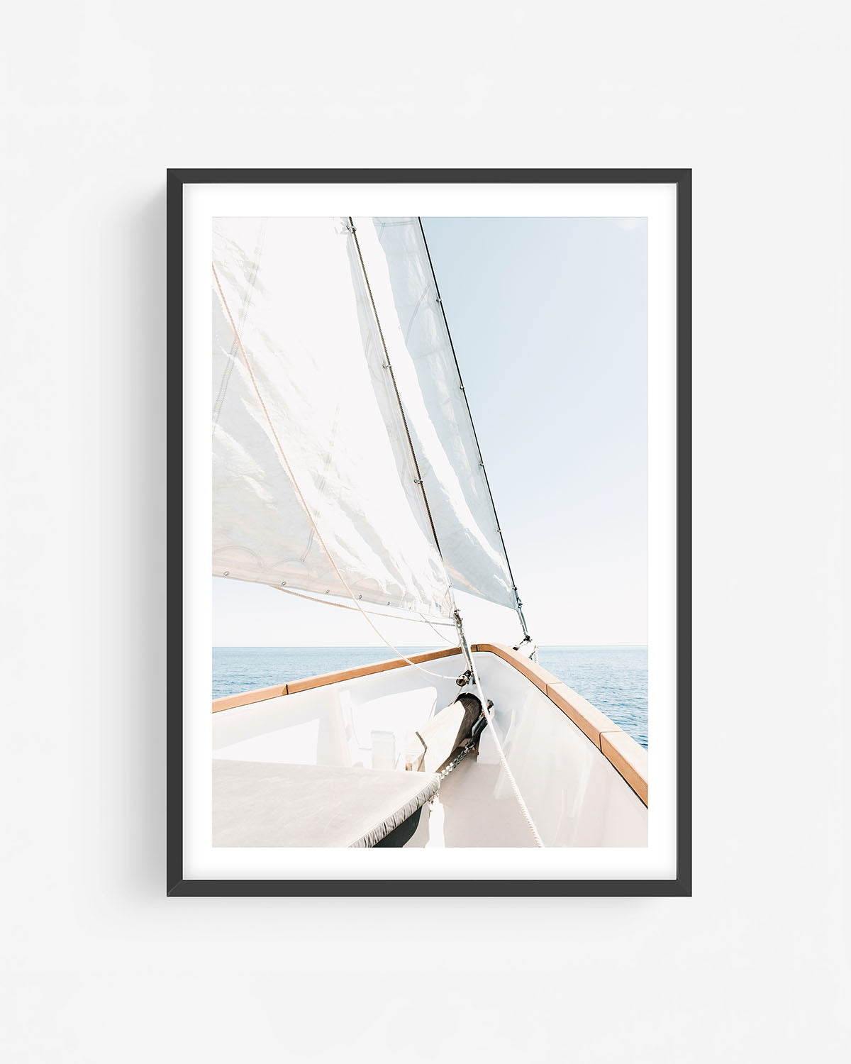 Fine art sailboat photograph in a black frame showing the bow of a sailboat with white sails and open ocean under a clear sky.