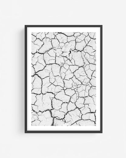 Black and white cracked earth texture photography in black frame showing dry desert ground pattern, minimalist abstract wall art print.