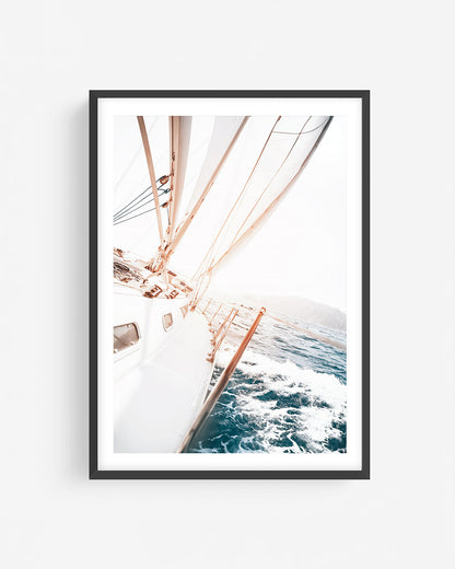 Fine art sailing photograph in a black frame showing a sailboat cutting through blue water with sunlit sails and dynamic ocean motion.