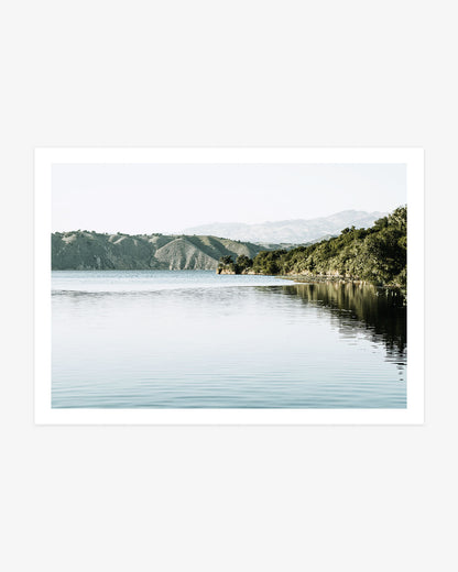 Lake Cachuma wall art featuring calm blue water, a wooded shoreline and layered hills beneath a pale Santa Ynez Valley sky.