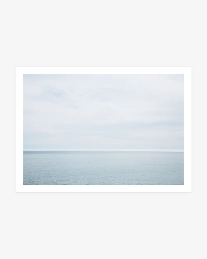 Big Sur minimalist ocean photography featuring calm blue Pacific water beneath an expansive, softly clouded sky along the California coast.