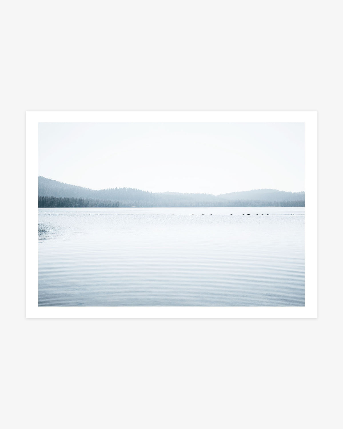 Northern California lake photography featuring calm blue water, gentle ripples and layered evergreen hills fading into a pale sky.