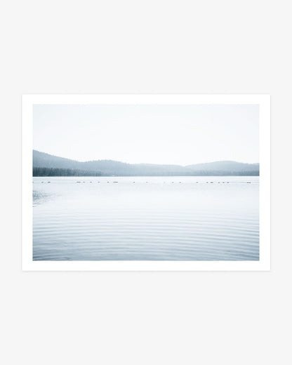 Northern California lake photography featuring calm blue water, gentle ripples and layered evergreen hills fading into a pale sky.