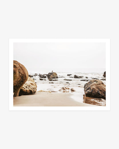 Malibu rocky beach photography featuring smooth coastal boulders, scattered ocean rocks and gentle Pacific waves beneath a pale sky.
