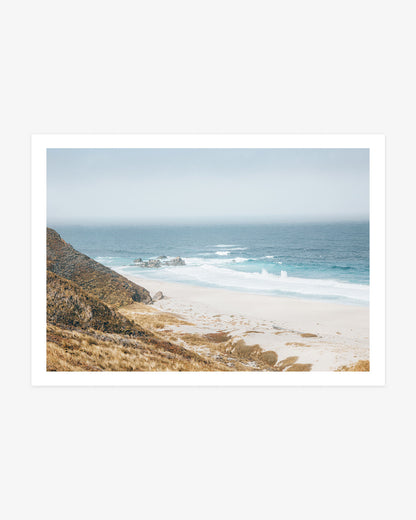 Big Sur coastal wall art featuring turquoise Pacific waves, a quiet sandy cove and golden California cliffs beneath a soft blue sky.