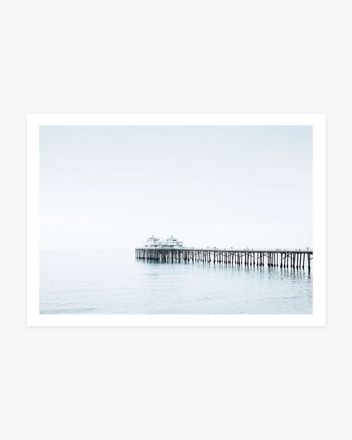 Minimalist Malibu Pier photography featuring the wooden pier extending across calm blue Pacific water beneath a bright, nearly seamless coastal sky.