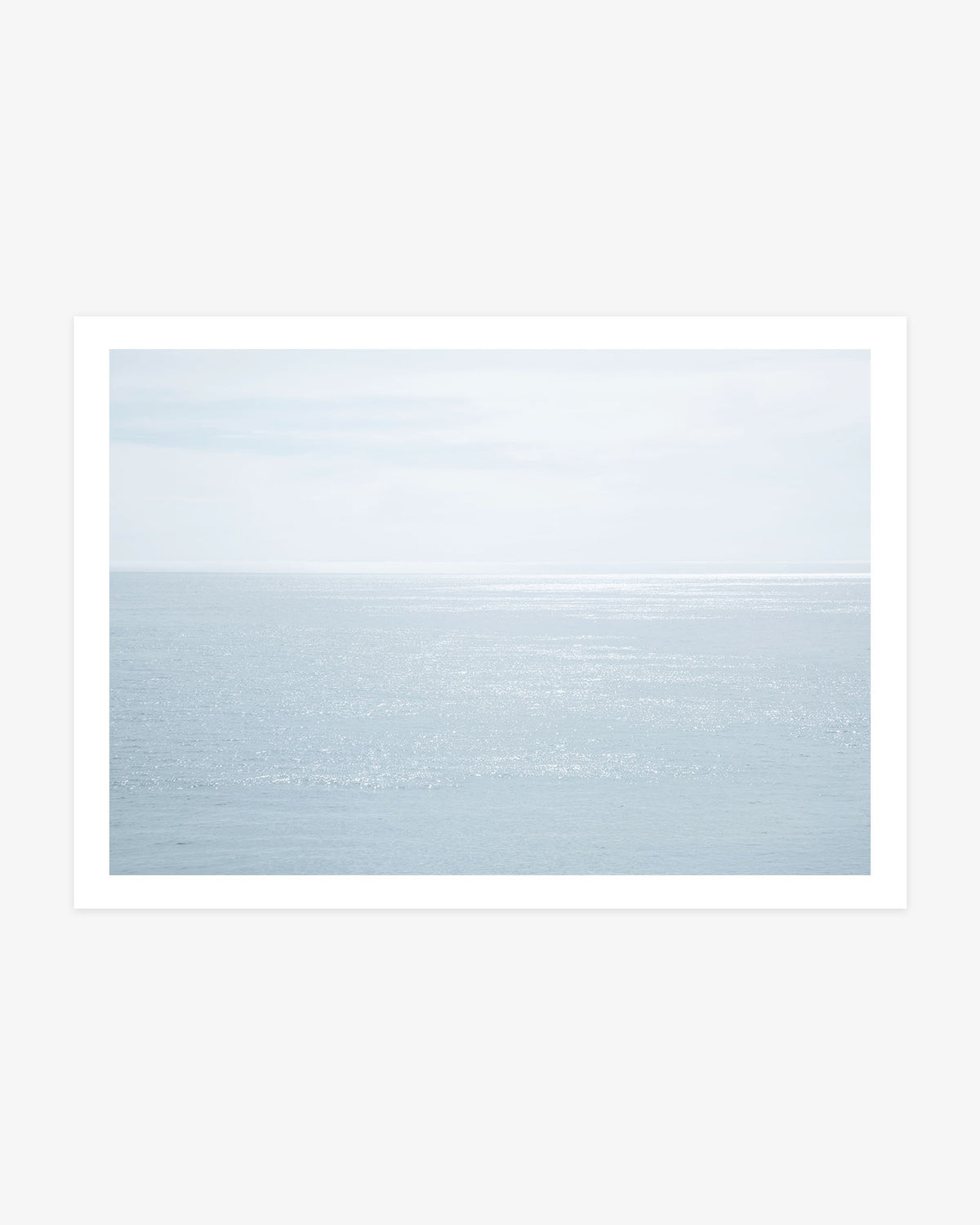 Malibu ocean photography featuring sunlight shimmering across calm blue Pacific water beneath a pale, softly clouded coastal sky.