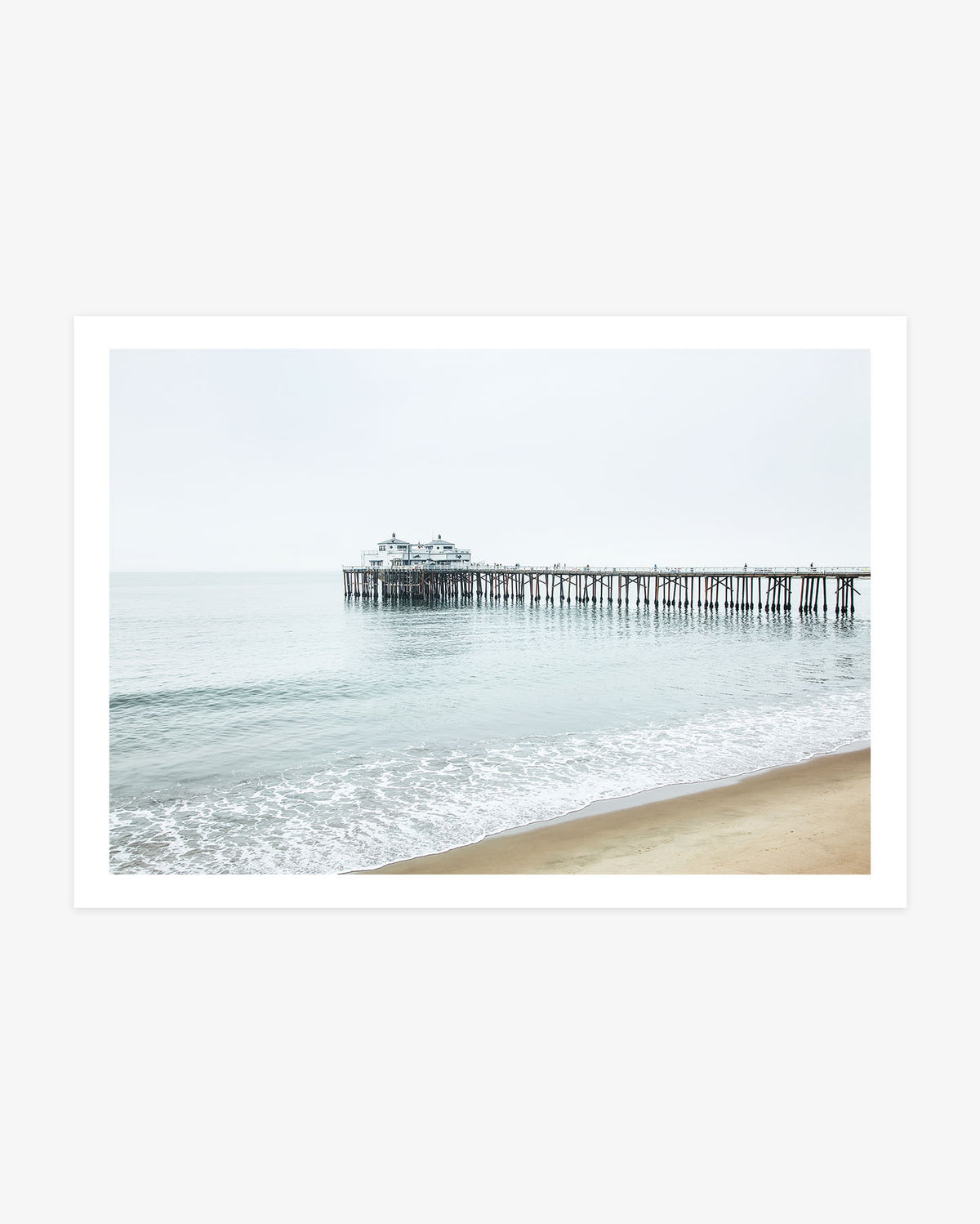 Malibu Beach wall art featuring Malibu Pier extending above calm Pacific water beside a softly curved sandy California shoreline.
