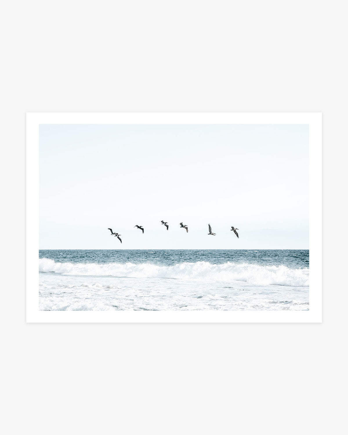Newport Beach coastal photography featuring a flock of pelicans flying above blue Pacific waves beneath a pale open sky.
