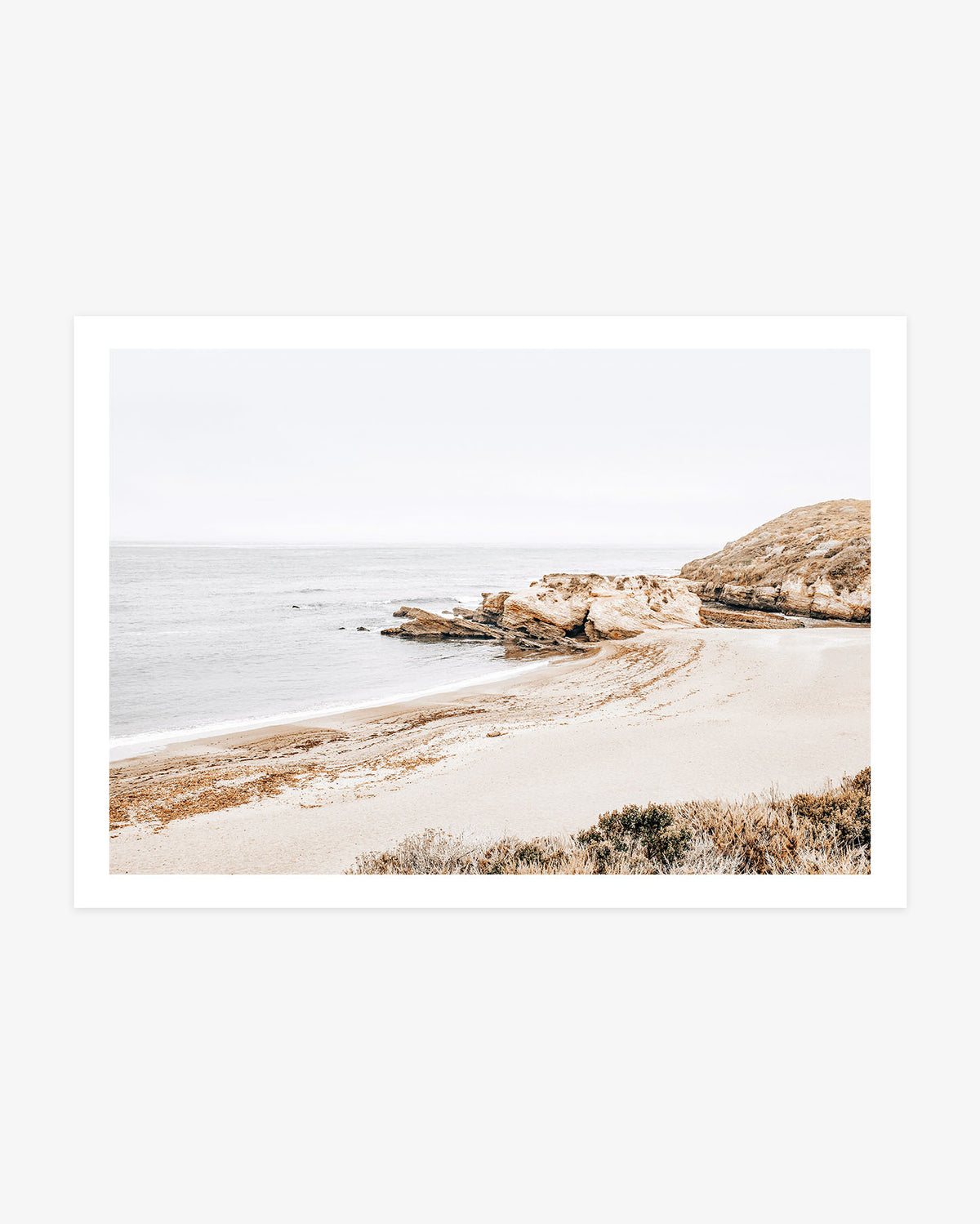 Montaña de Oro wall art featuring a quiet sandy cove, layered coastal rock formations and calm Pacific water beneath a pale California sky.