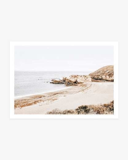 Montaña de Oro wall art featuring a quiet sandy cove, layered coastal rock formations and calm Pacific water beneath a pale California sky.