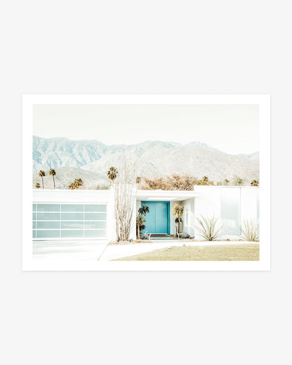 White mid-century modern Palm Springs home with a turquoise front door, desert landscaping, palm trees, and mountain views.