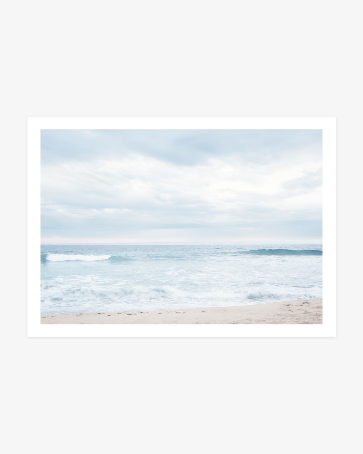 Newport Beach ocean photography featuring soft blue waves rolling toward a pale sandy shore beneath a bright, cloud-filled sky.