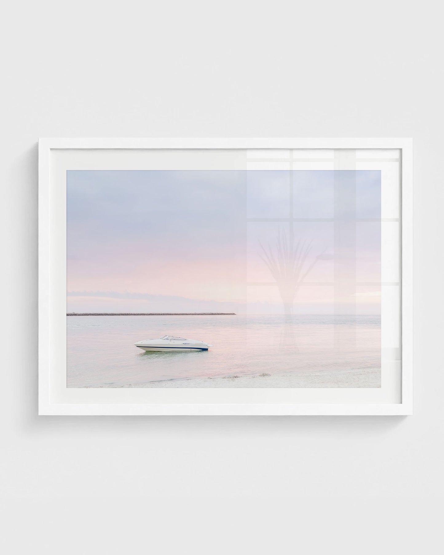 Clearwater Beach sunset wall art featuring a small white boat floating on calm water with a soft pastel pink and blue sky and a distant shoreline, framed in a white frame.