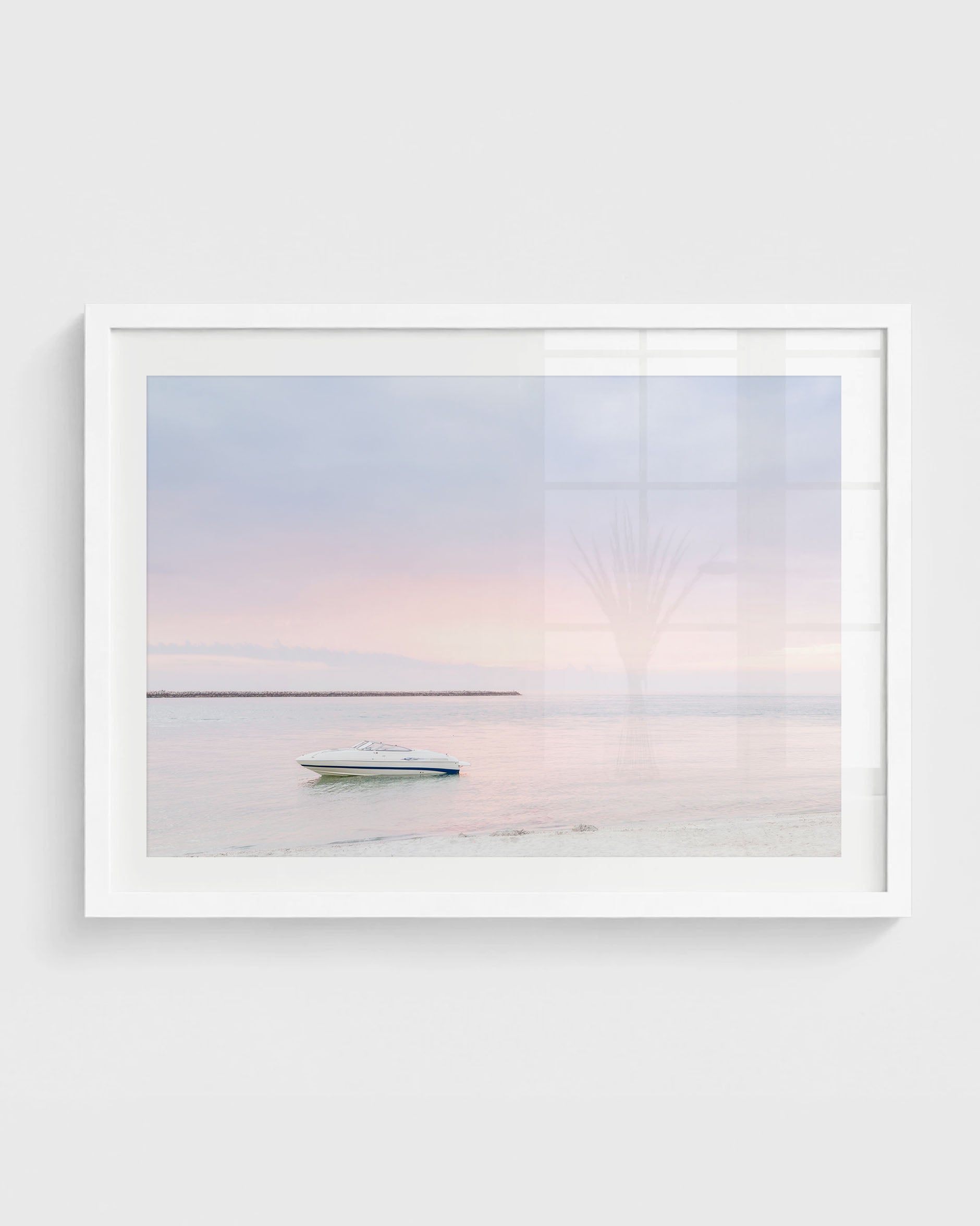 Clearwater Beach sunset wall art featuring a small white boat floating on calm water with a soft pastel pink and blue sky and a distant shoreline, framed in a white frame.