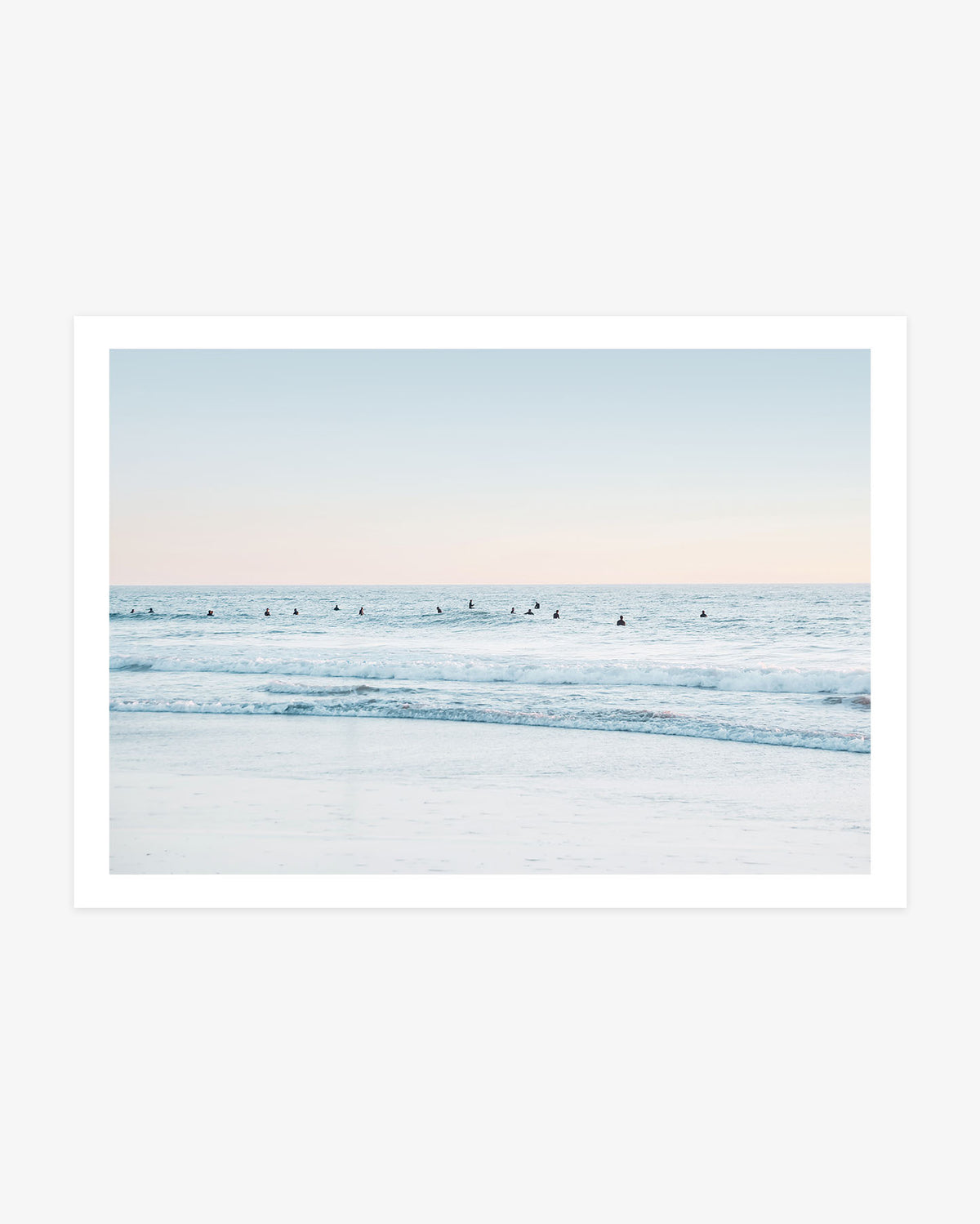 San Clemente surf wall art featuring a wide lineup of surfers waiting in pale blue Pacific water beneath a soft blush coastal sky.