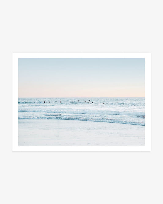 San Clemente surf wall art featuring a wide lineup of surfers waiting in pale blue Pacific water beneath a soft blush coastal sky.