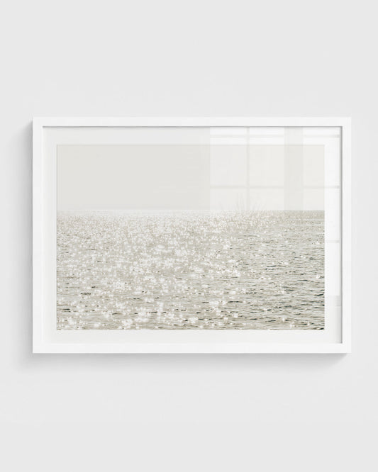 Sunlight reflecting on calm ocean water wall art in neutral coastal tones.