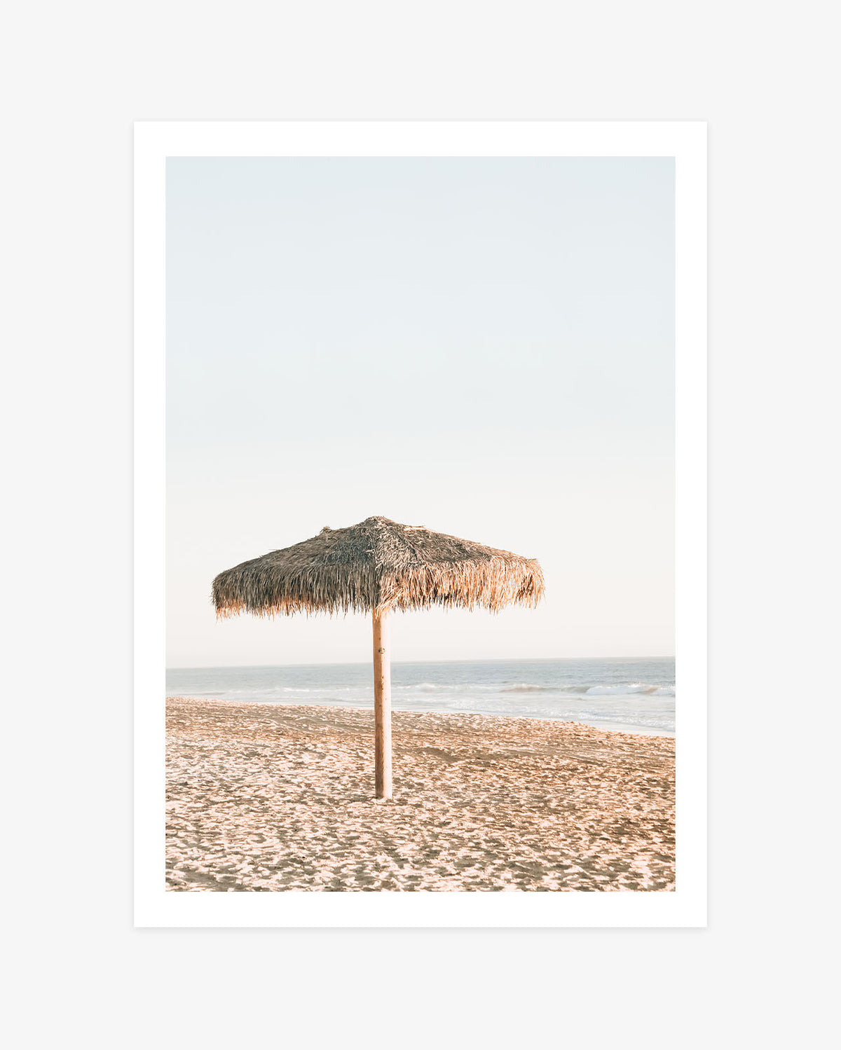 San Clemente beach wall art featuring a lone thatched palapa on warm sand beside the calm Pacific Ocean beneath a pale blue sky.