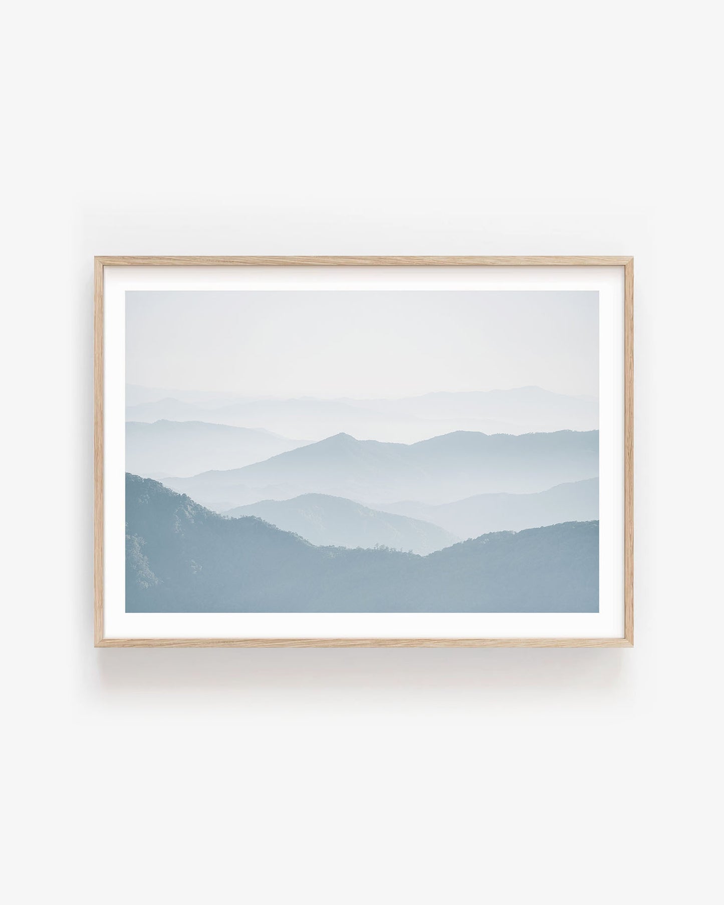 Minimalist foggy mountain landscape in soft blue tones, showing gentle overlapping ridges and atmospheric mist modern calming wall art print.