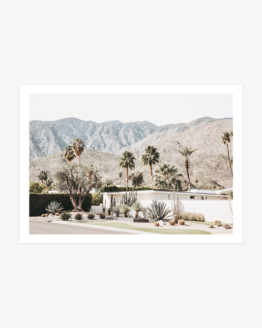 White mid-century modern Palm Springs home surrounded by agaves, cacti, palm trees, and the rugged San Jacinto Mountains.
