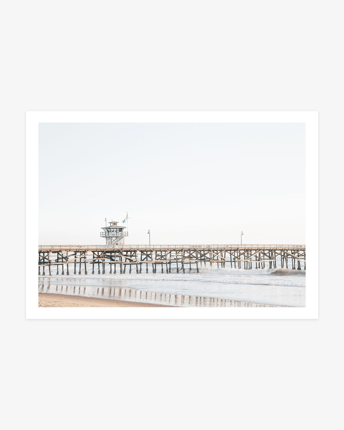 San Clemente Pier wall art featuring the wooden pier above gentle Pacific waves beneath a pale blue Southern California sky.
