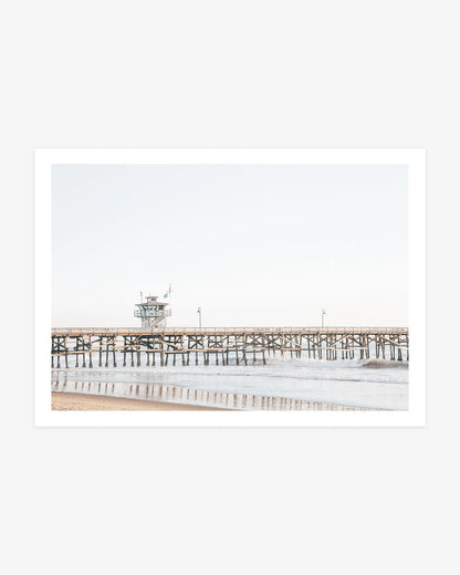 San Clemente Pier wall art featuring the wooden pier above gentle Pacific waves beneath a pale blue Southern California sky.