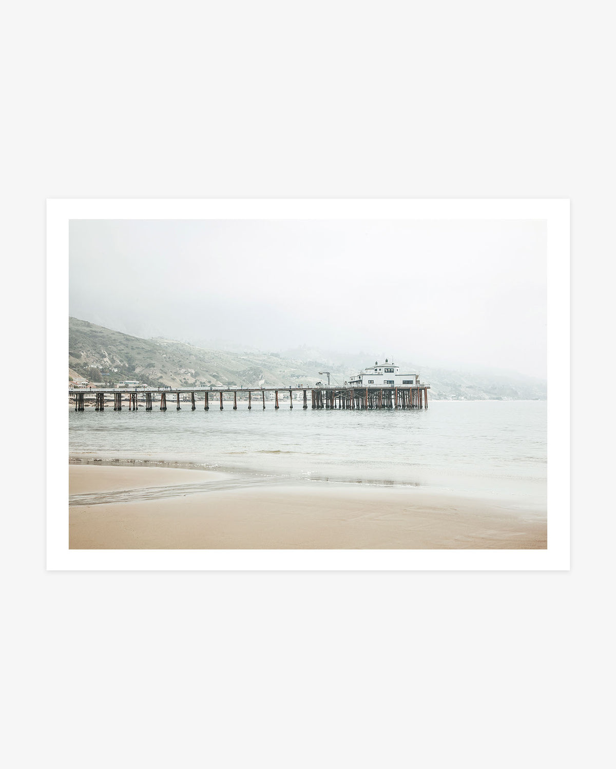 Malibu Pier photography featuring the historic wooden pier extending across calm Pacific water beneath soft coastal mist and pale California hills.