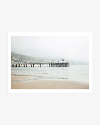 Malibu Pier photography featuring the historic wooden pier extending across calm Pacific water beneath soft coastal mist and pale California hills.