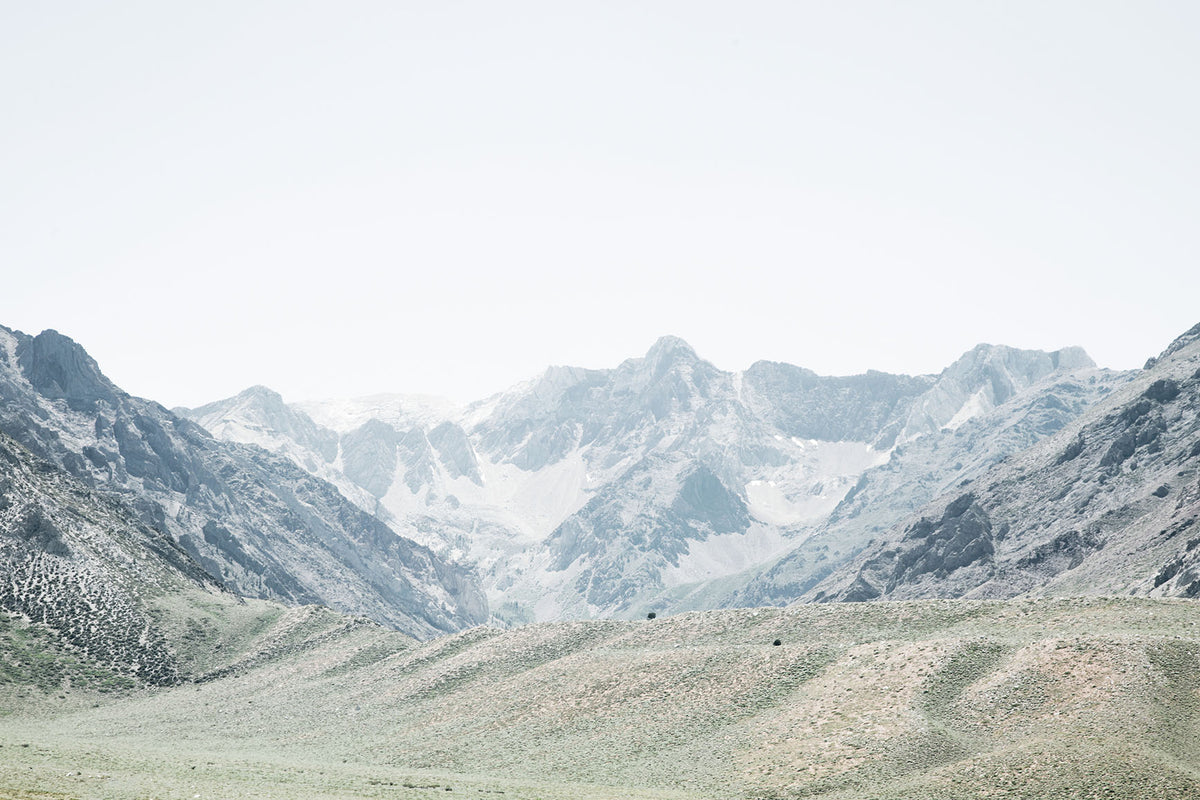 Sierra Nevada landscape photography featuring expansive green foothills beneath dramatic rugged mountain peaks in soft, muted tones.