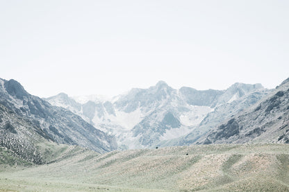 Sierra Nevada landscape photography featuring expansive green foothills beneath dramatic rugged mountain peaks in soft, muted tones.