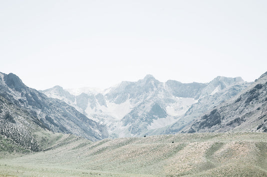 Sierra Nevada landscape photography featuring expansive green foothills beneath dramatic rugged mountain peaks in soft, muted tones.