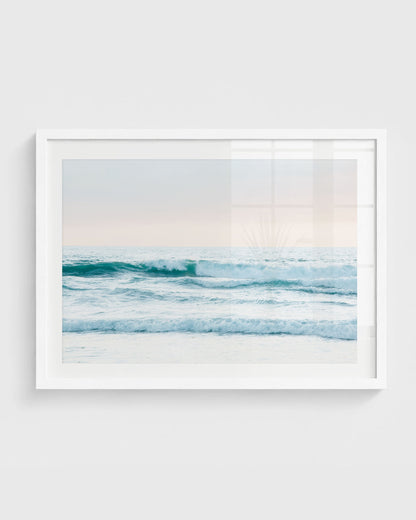 Ocean waves wall art featuring soft rolling waves in blue tones under a pastel sky with a clean horizon line, framed in a white frame.