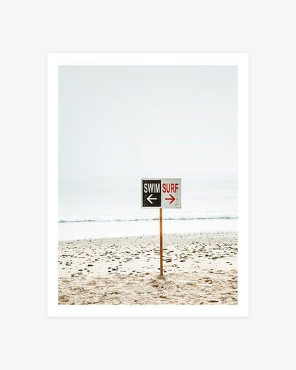Malibu Beach photography featuring a weathered swim and surf sign standing on a pale sandy shore beside the Pacific Ocean.