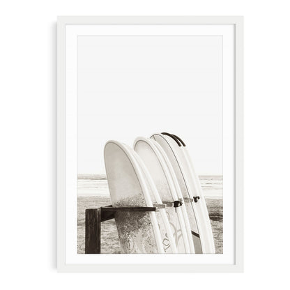 Minimalist beach wall art featuring multiple surfboards organized in a wooden surfboard stand near the sand with neutral beige tones and soft coastal lighting.