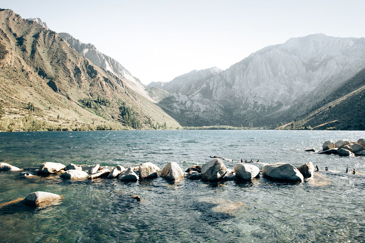 Convict Lake landscape with clear blue water, shoreline boulders, and dramatic Sierra Nevada mountains rising in the distance.