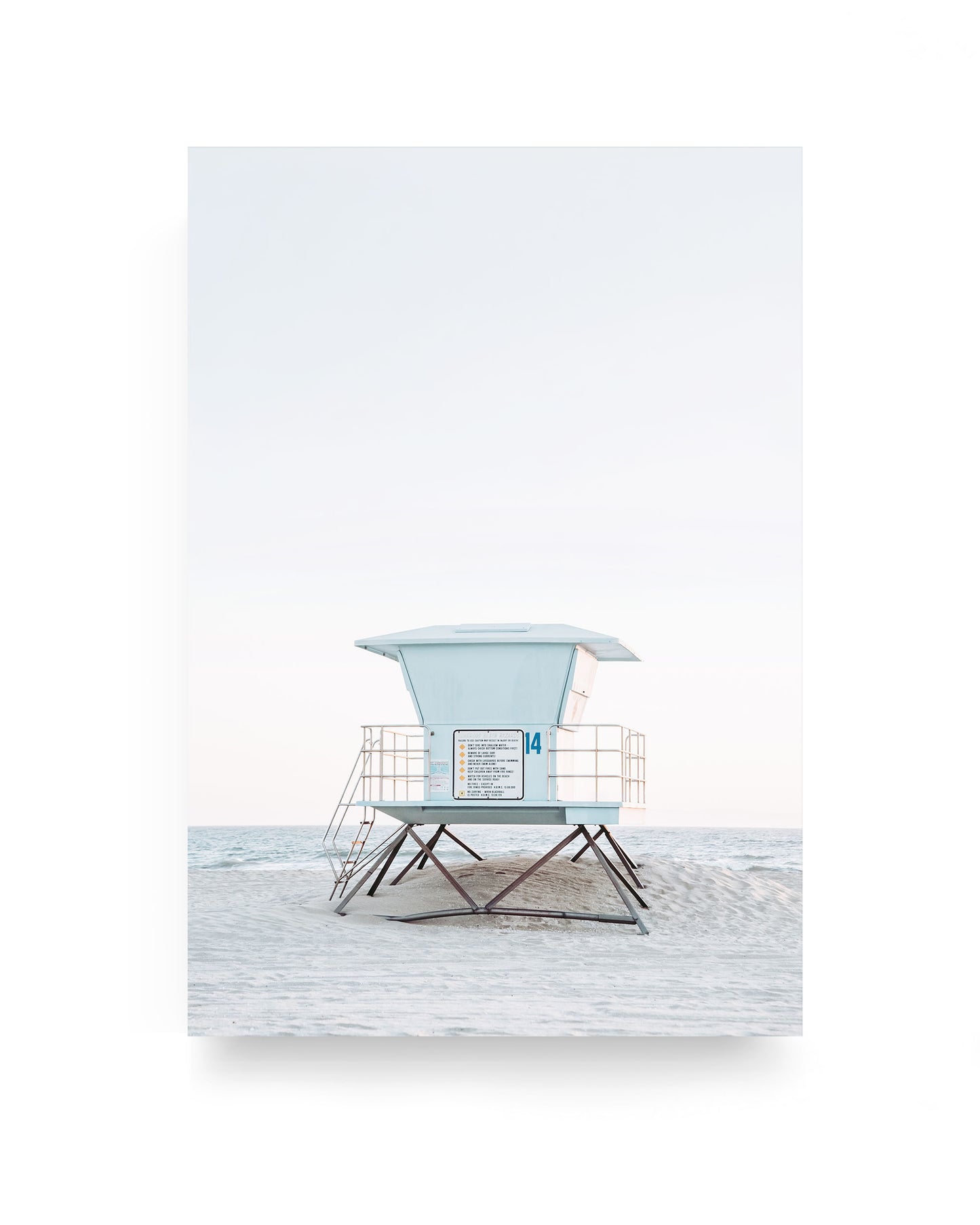 Pastel blue lifeguard tower number 14 on Huntington Beach standing on pale sand with calm ocean horizon and soft minimalist sky, coastal beach photography with clean neutral tones.