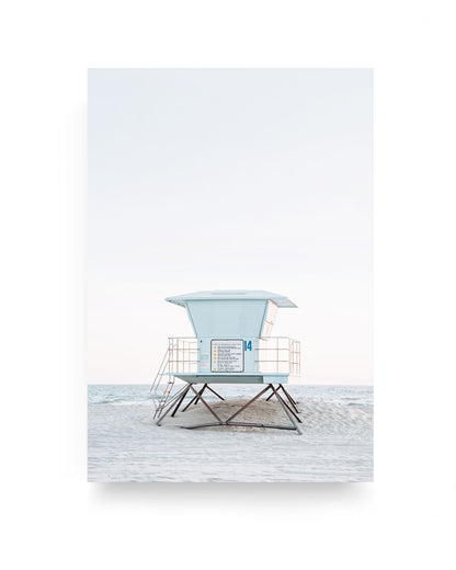 Pastel blue lifeguard tower number 14 on Huntington Beach standing on pale sand with calm ocean horizon and soft minimalist sky, coastal beach photography with clean neutral tones.