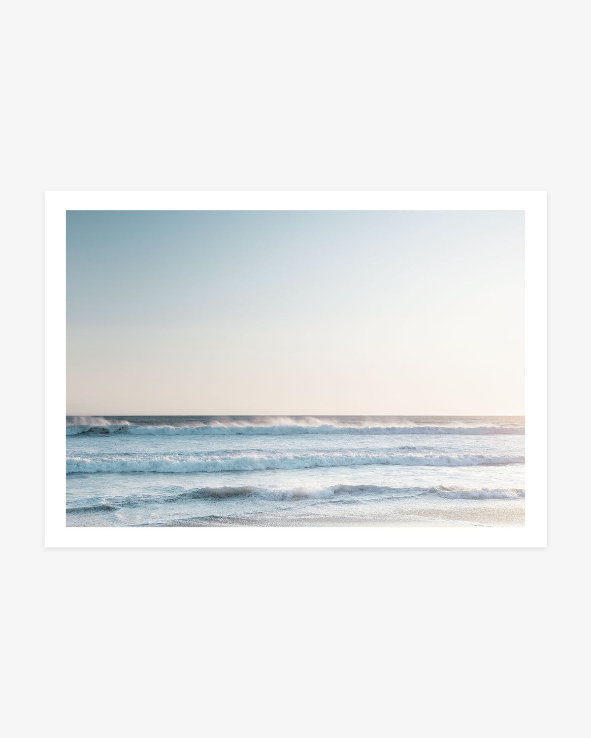 Pacific Ocean wall art featuring layered blue waves rolling toward shore beneath a softly lit neutral coastal sky.
