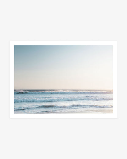 Pacific Ocean wall art featuring layered blue waves rolling toward shore beneath a softly lit neutral coastal sky.