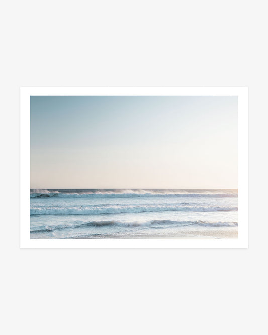 Pacific Ocean wall art featuring layered blue waves rolling toward shore beneath a softly lit neutral coastal sky.